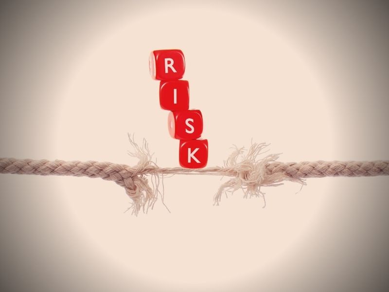 Dice saying "risk" dangling off of a thin piece of rope, clearly close to falling.