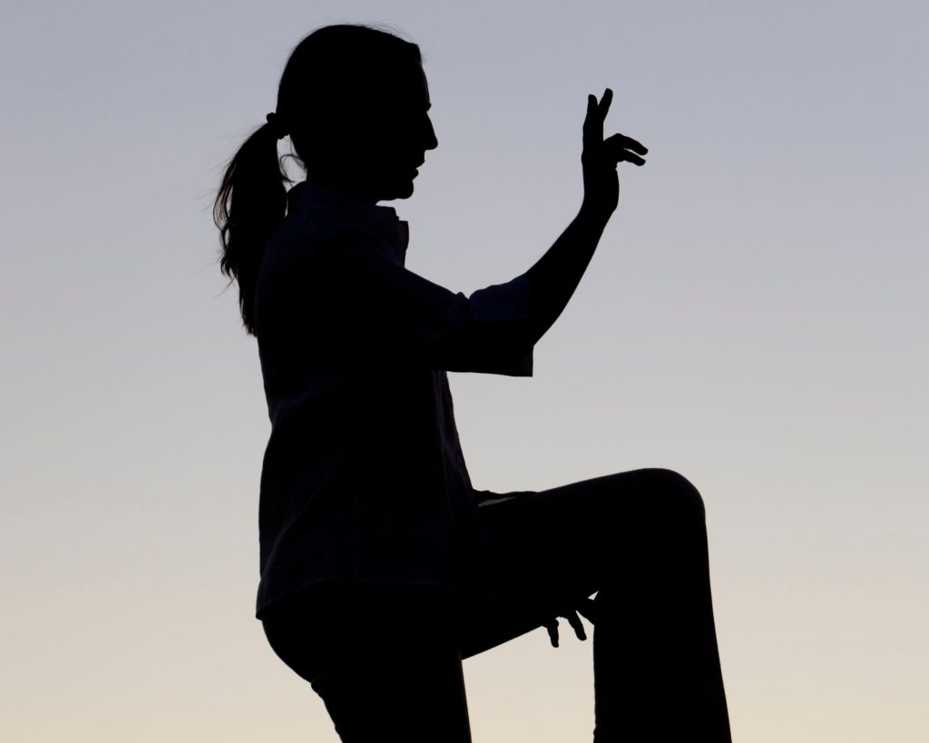 A woman practicing a complex tai chi movement.