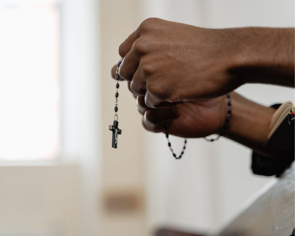 A pair of hands clutching a Catholic rosary at Church.